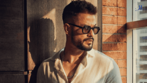Kunal Kemmu, host of Prime Video's Alliance, poses in sunglasses and a white shirt against a sunlit brick wall