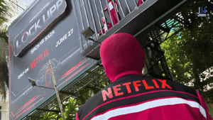 Lock Upp Sach Ya Saza Netflix guerrilla marketing campaign — masked prisoner in red Netflix uniform stands in front of Lock Upp Season 2 billboard announcing June 27 premiere