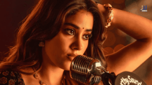 Janhvi Kapoor as Achiyamma in a warm-lit close-up scene from the 2026 Telugu film Peddi, styled in traditional jewellery with a vintage microphone in the foreground