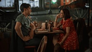 Nick Robinson and Zoey Deutch share a warm moment over drinks at a restaurant in a scene from Voicemails for Isabelle on Netflix