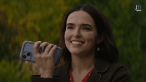 Zoey Deutch as Jill holds a phone to her ear while smiling outdoors in a still from Voicemails for Isabelle (2026) on Netflix